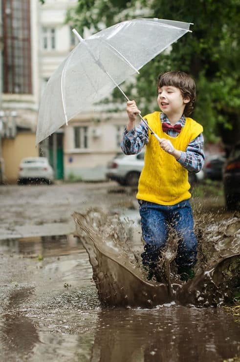 A boy playing in a puddle of water on a street after rain and flooding