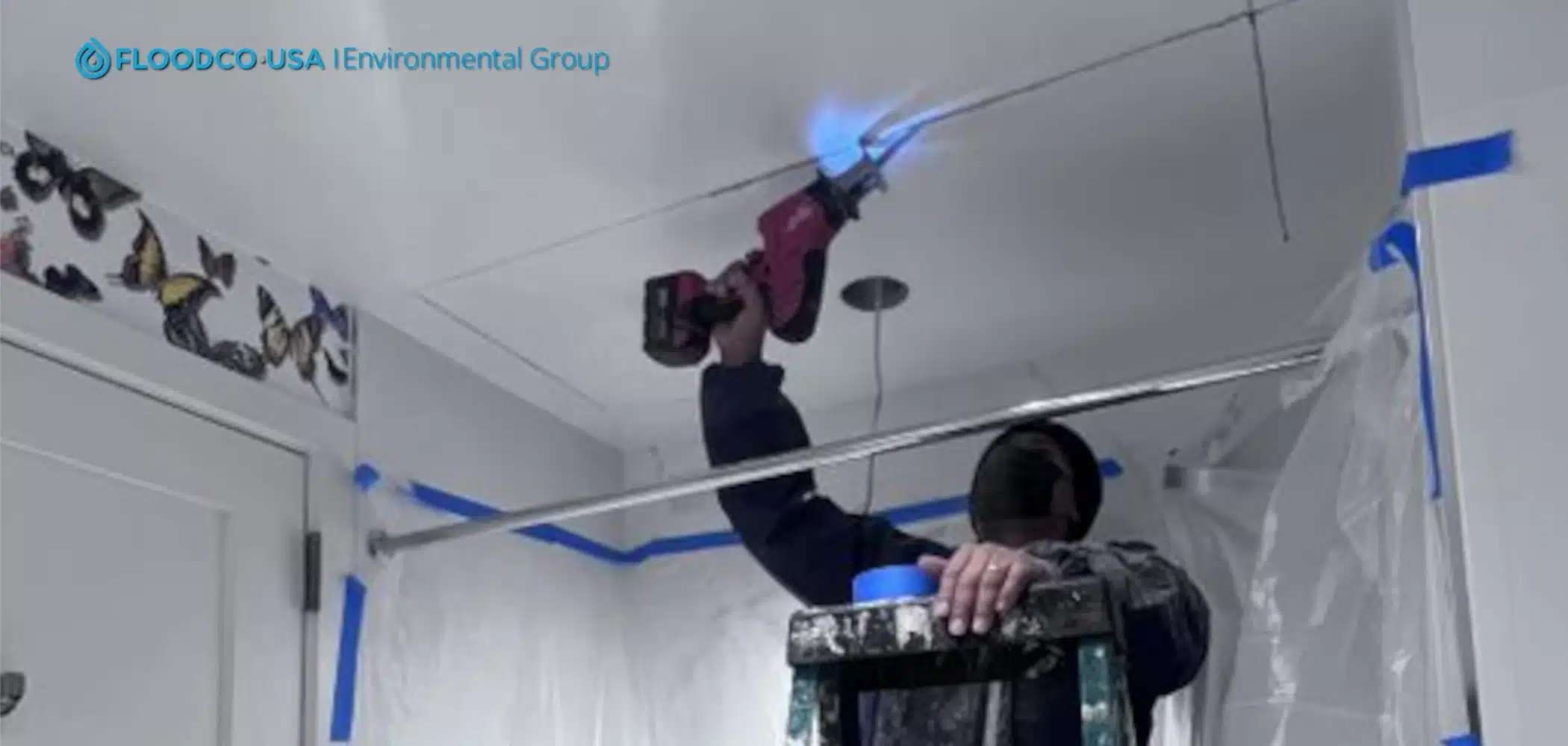 FloodCo expert on a ladder surrounded by plastic to protect the area while drilling to test for mold