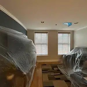 Room prepared for duct cleaning with furniture covered in plastic, highlighting professional setup before the job.